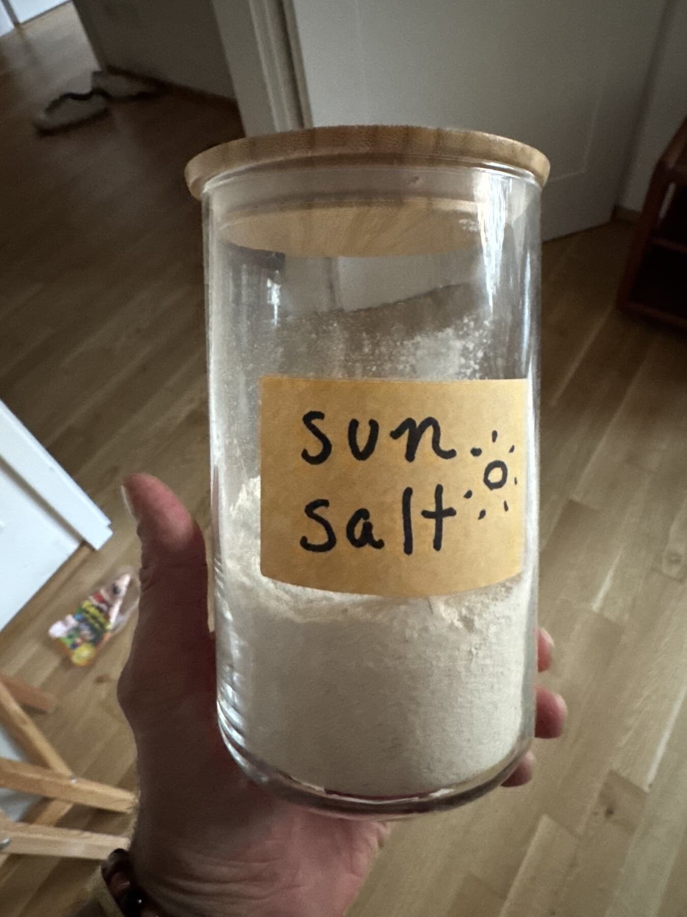 Justin holding the first jar of homemade Sun Salt, a pale lemon mineral powder in a glass jar with a bamboo lid and handwritten label.